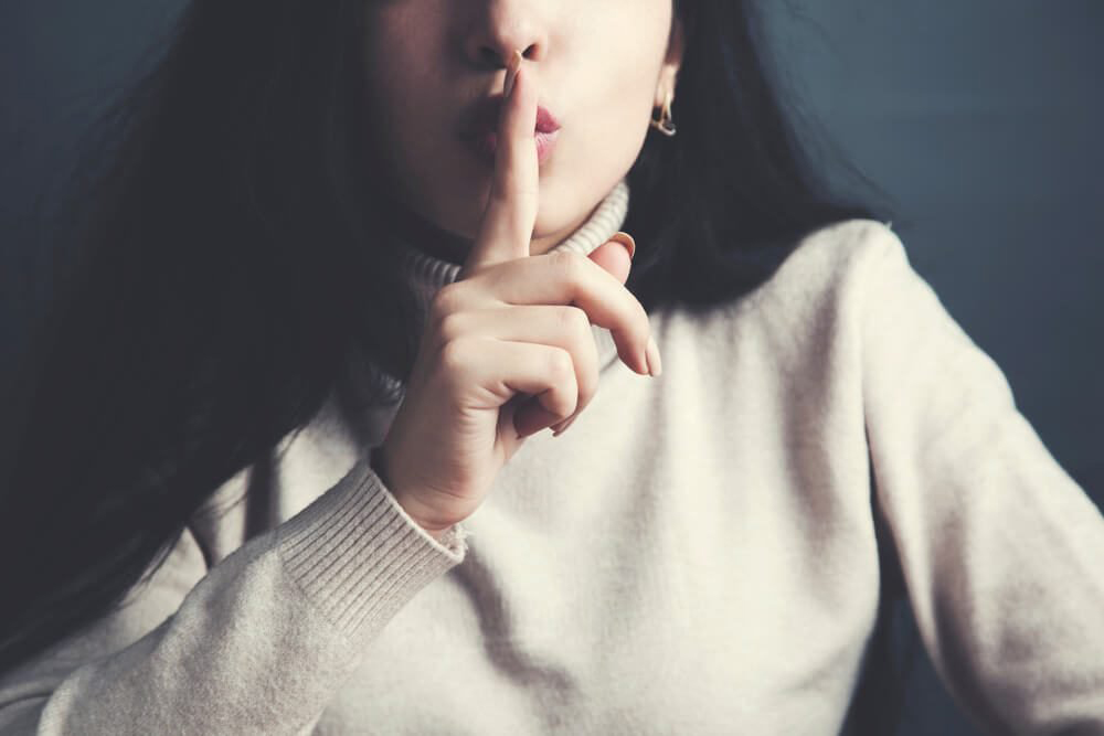 A woman in white with cautioning finger on mouth